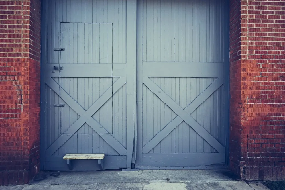 Pair of gray-blue wooden carriage-style doors with crossbuck bracing in a brick opening