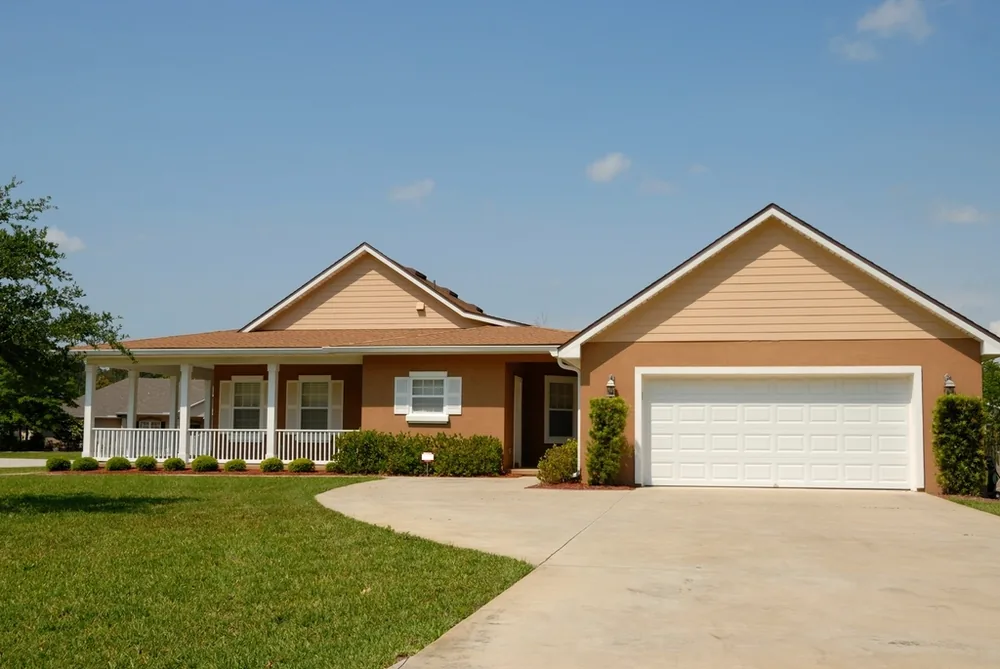 Single-story ranch house with a white two-car steel garage door at the end of a curved drive