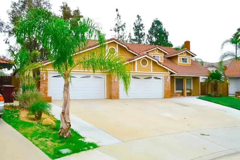 Two-story stucco house with two white raised-panel garage doors behind a wide concrete driveway
